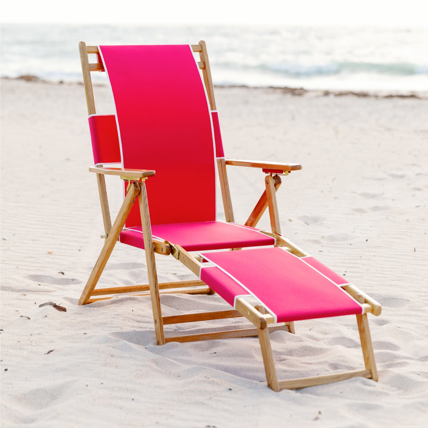 Coastsetter Beach Chair in Jockey Red reclined on the sand with the leg rest extended