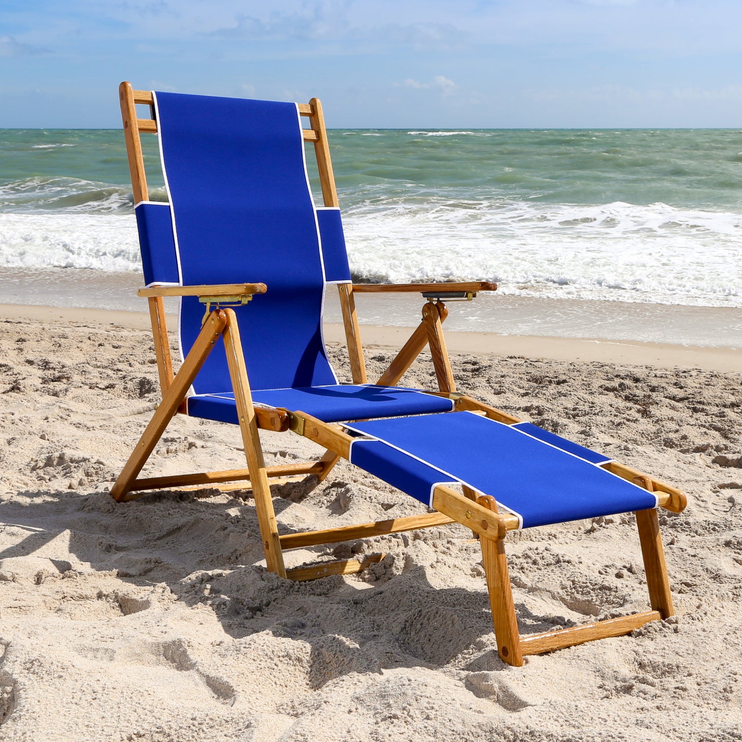 Coastsetter Beach Chair in Pacific Blue reclined on the sand with the leg rest extended