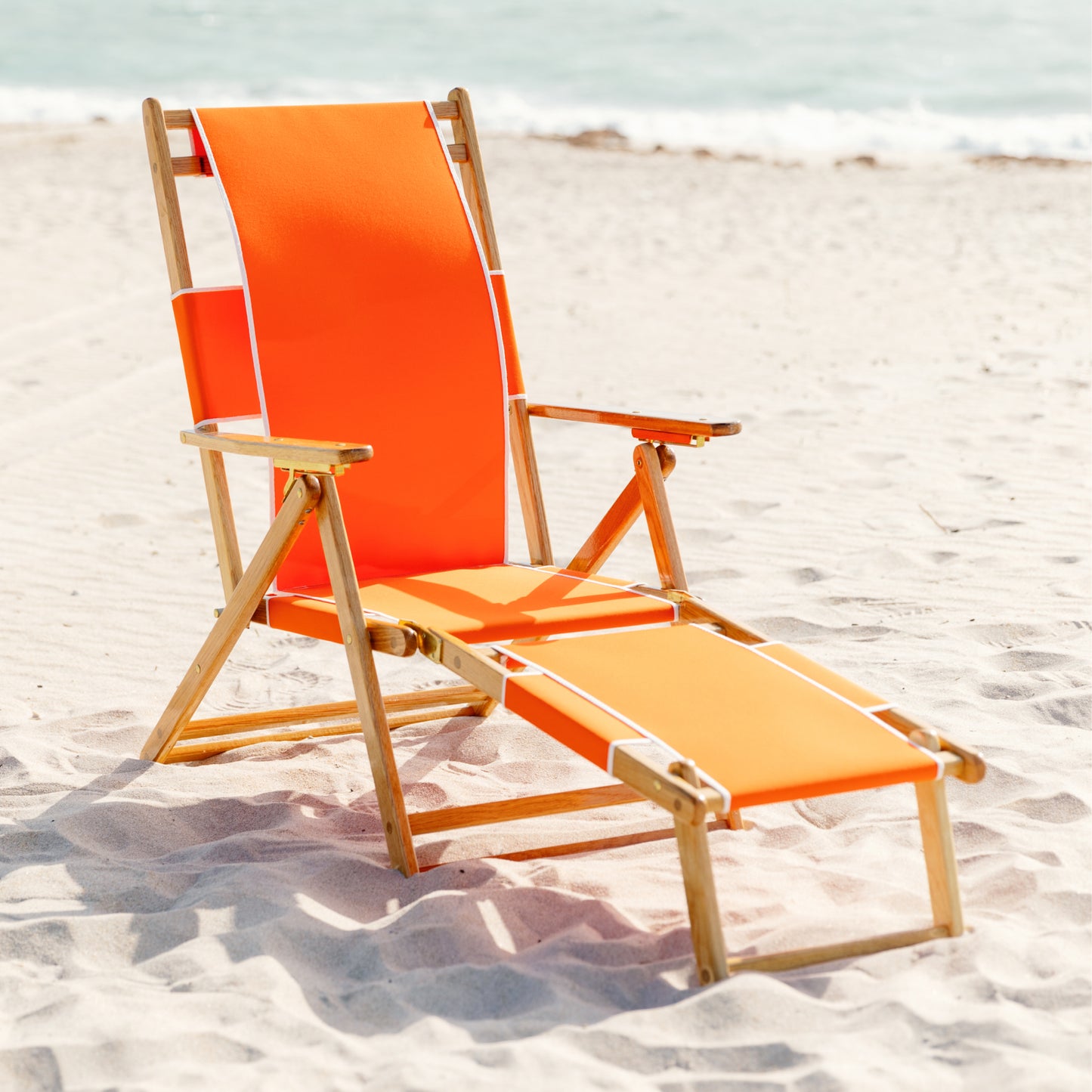 Coastsetter Beach Chair in Tangerine reclined on the sand with the leg rest extended