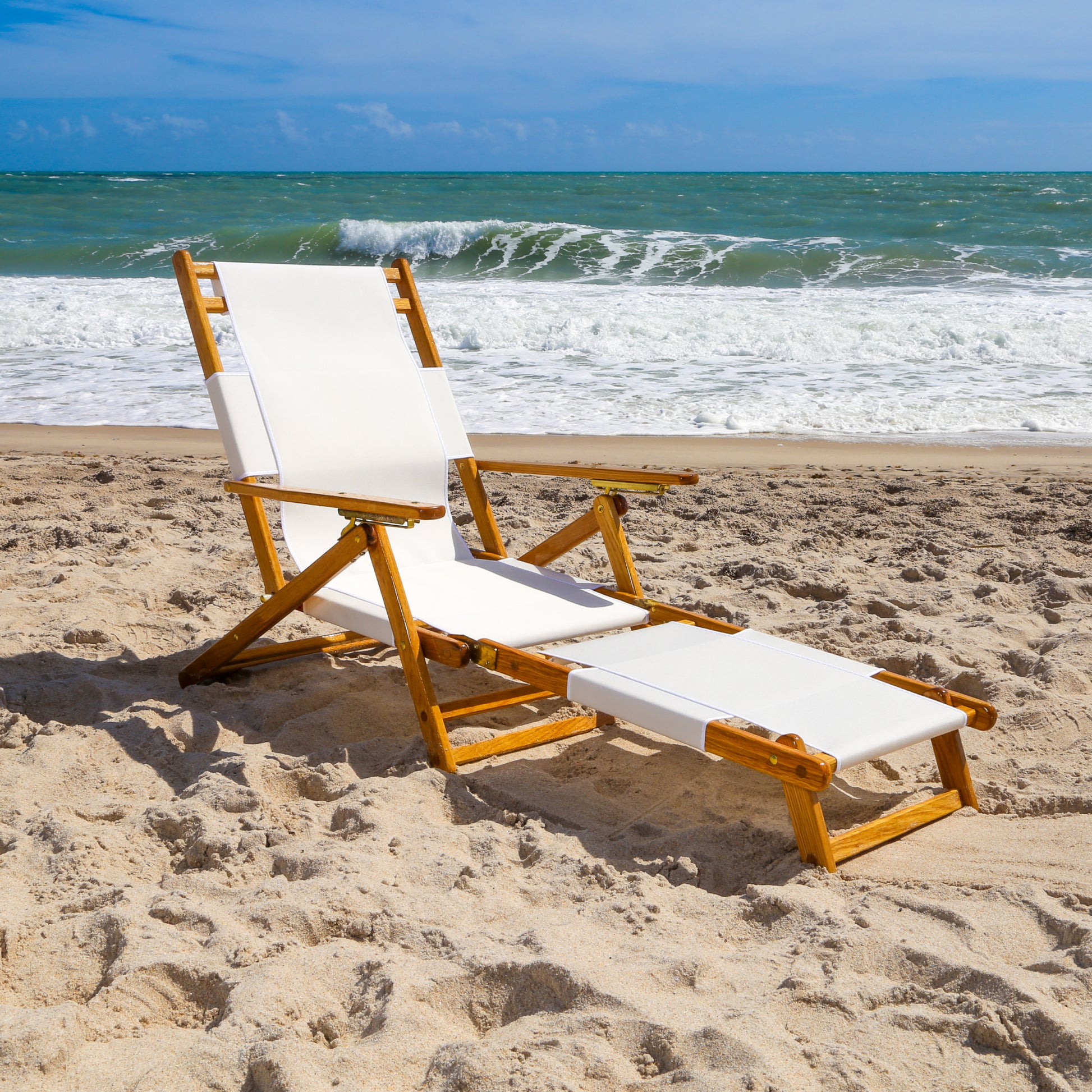 Coastsetter Lounge Chair in White reclined on the sand with the leg rest extended