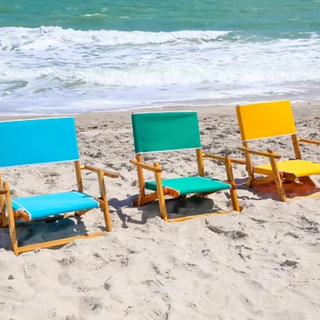 Three Coastsetter Sand Chairs in turquoise, teal and yellow lined up on the beach